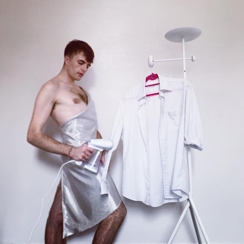 gorgeous man in a silver dress steaming a shirt